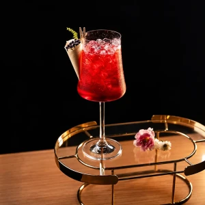 Aurora Spritz vermelho em taça de haste sobre um suporte dourado, com uma flor rosa ao lado