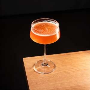 Golden Peach dourado em taça coupé de haste, sobre uma bancada de madeira