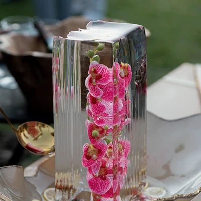 Bloco alto de gelo transparente com orquídeas rosa congeladas dentro, sobre bandeja branca