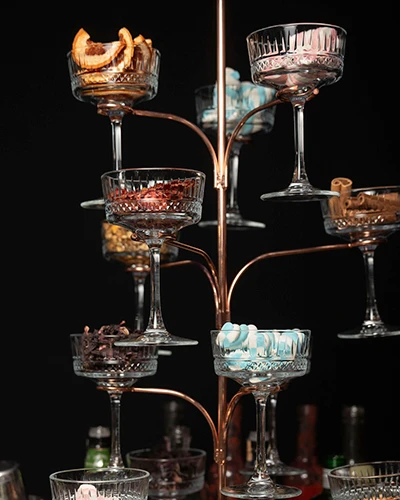 Suporte de cobre em forma de árvore com taças coupé de cristal cheias de guarnições, como frutas desidratadas, canela e balas