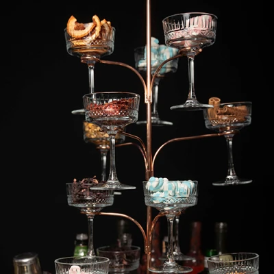 Suporte de cobre em forma de árvore com taças coupé de cristal cheias de guarnições, como frutas desidratadas, canela e balas